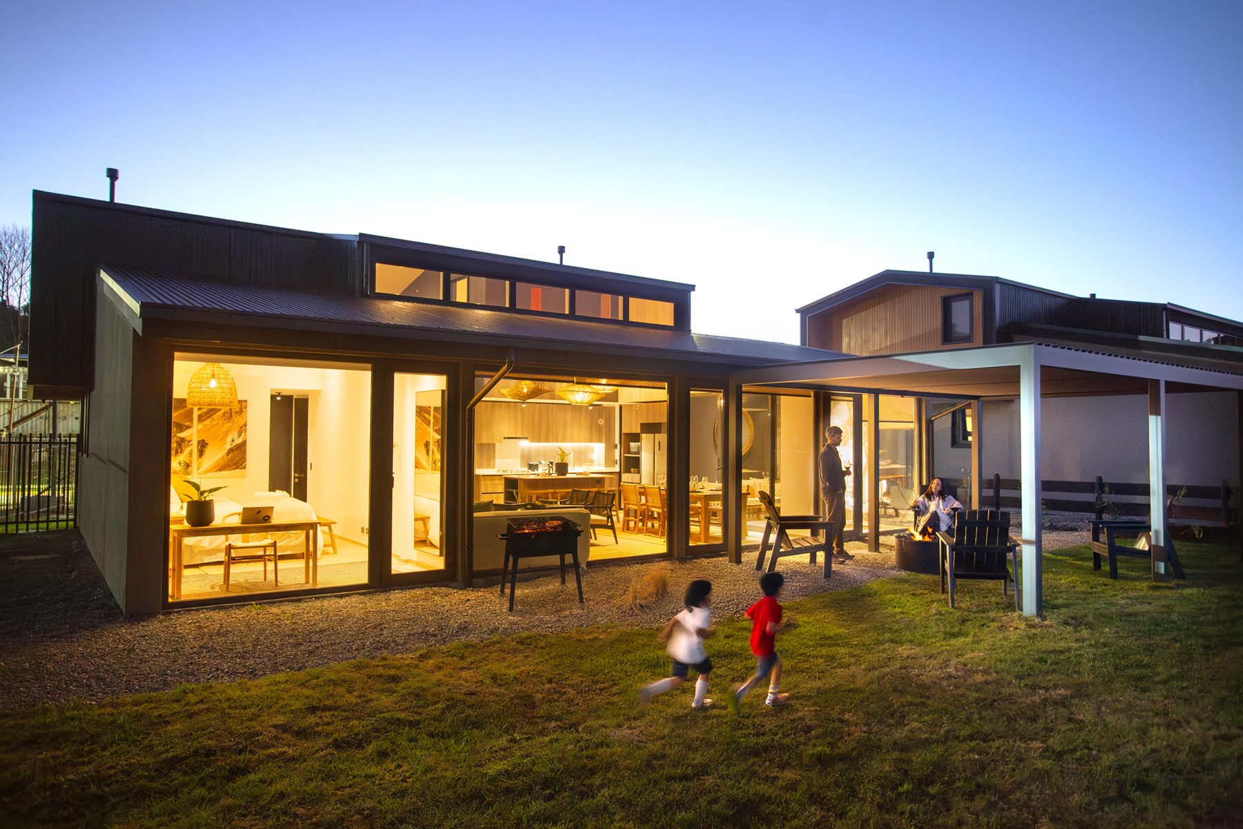 Casa del condominio al atardecer, con ventanales iluminados, terraza y jardín